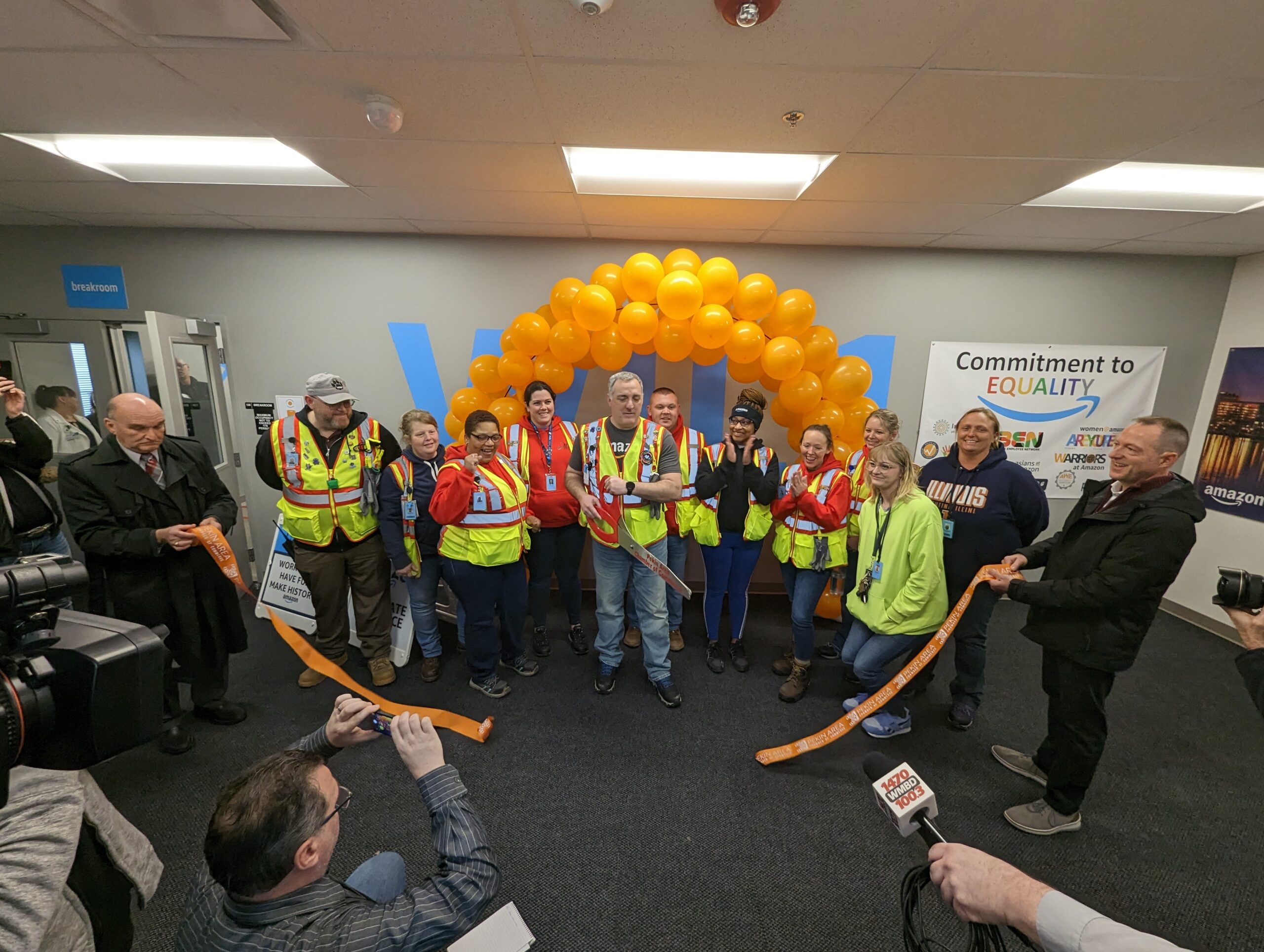 Group of people standing in front of balloons at a ribbon cutting ceremony at an Amazon fulfillment facility