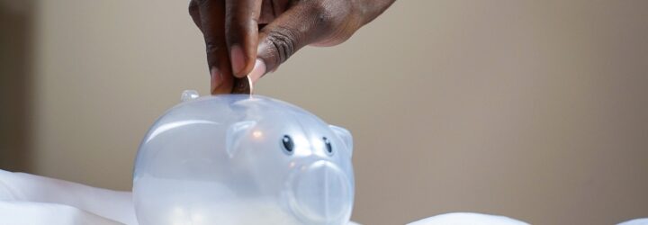 A hand putting money into a piggybank.